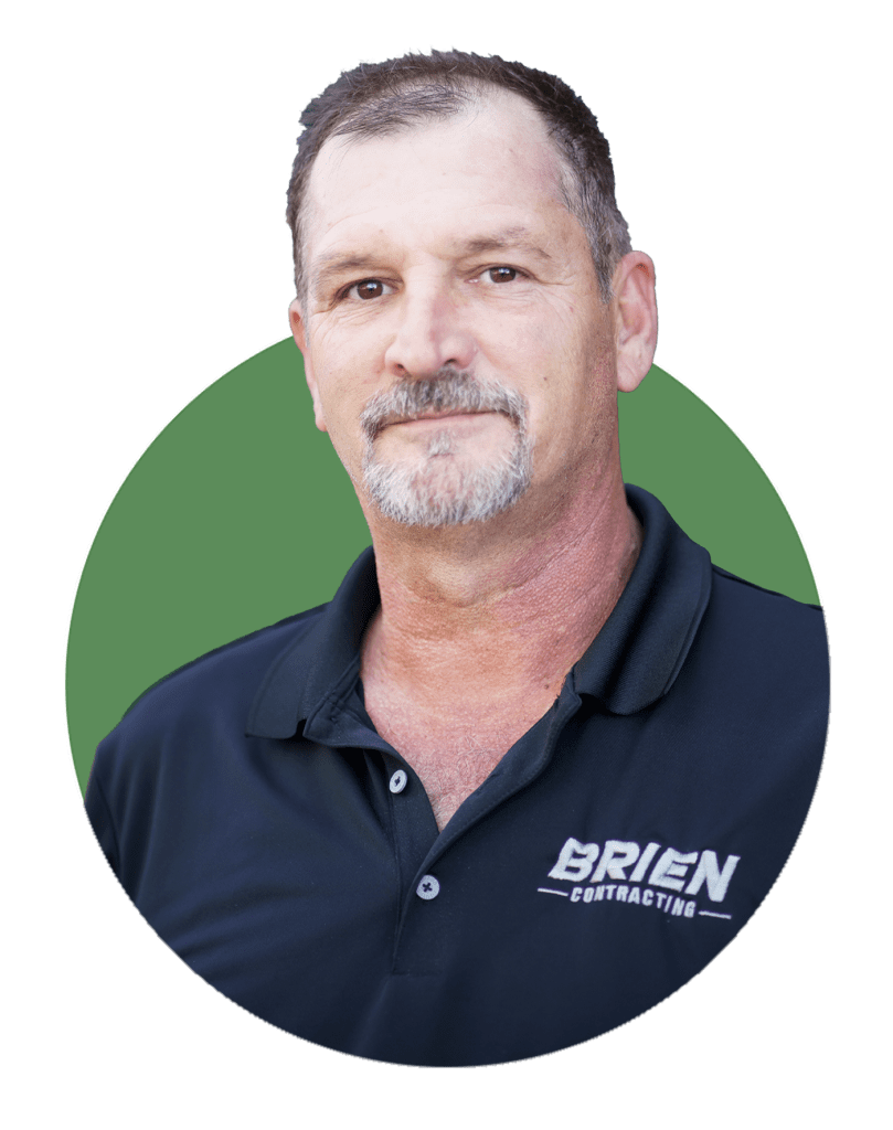 A middle-aged man with short hair and a goatee, wearing a dark polo shirt with the "Brien Contracting" logo—a trusted Arizona commercial contractor—stands in front of a green circular background.