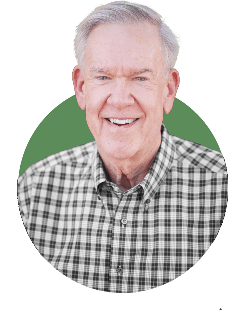 Smiling older man with gray hair, wearing a black and white plaid shirt, poses confidently in front of a green background—a trusted Arizona commercial contractor ready to help with your next project.