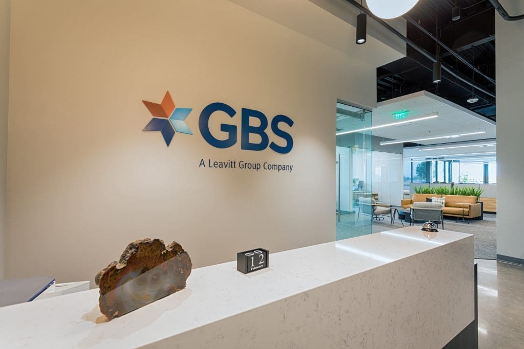 GBS Benefits Rivulon Gilbert Reception Desk with branded signage behind and decorations on the desk. Can also see part of the office in the background including a secondary seating area.