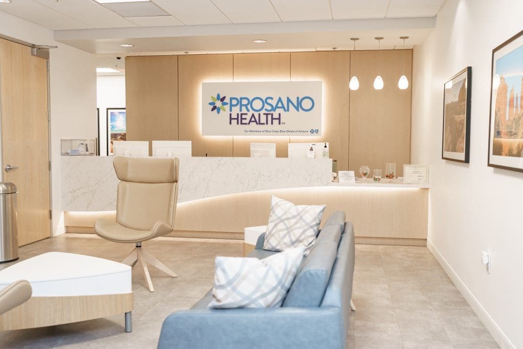 medical office patient waiting ares and check-in desk with Prosano Healthcare signage backlit behind it on a wood accent wall.