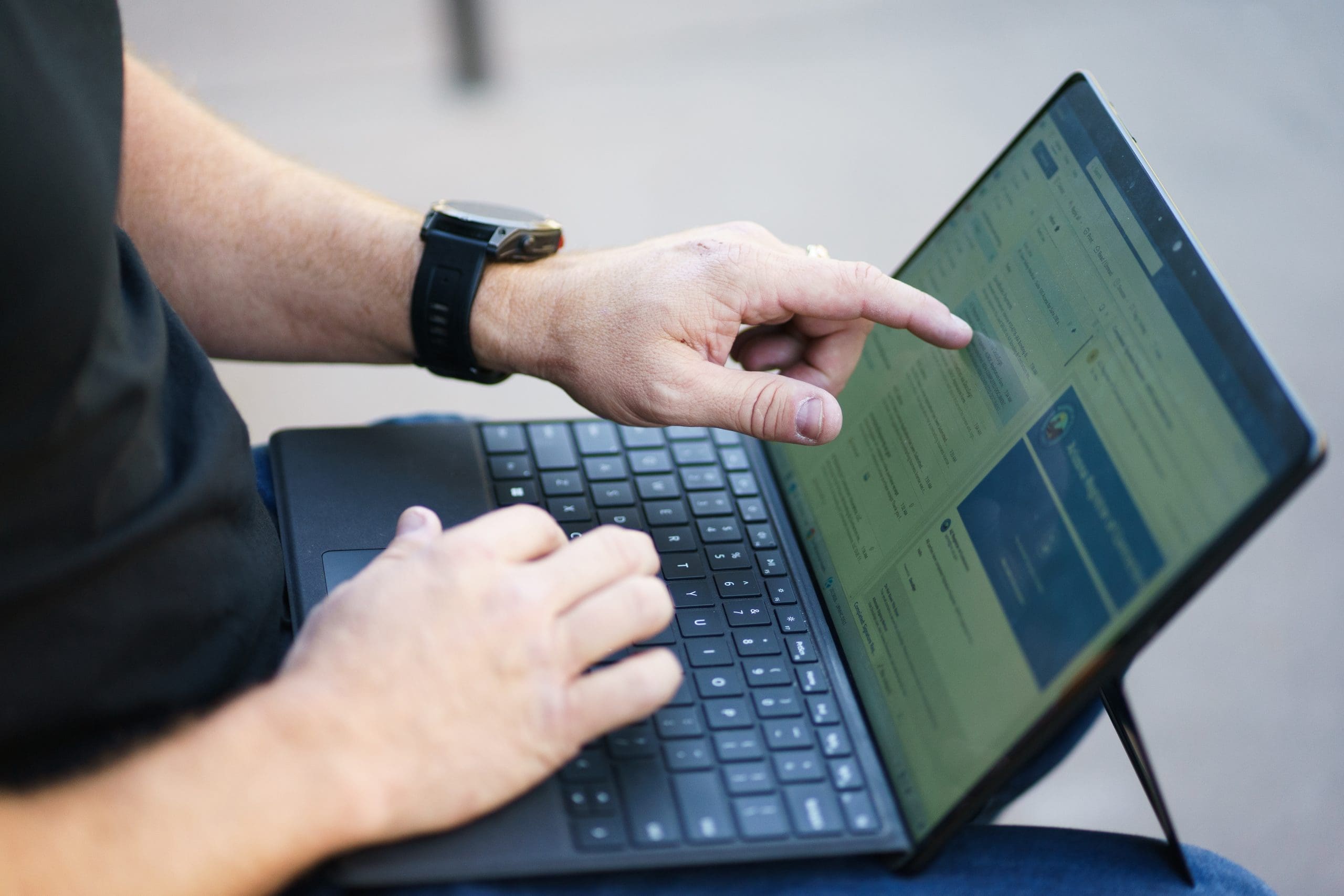 A person uses a tablet with a keyboard attached, typing with one hand and pointing at the screen with the other, perhaps researching why clean job sites save lives – and money.