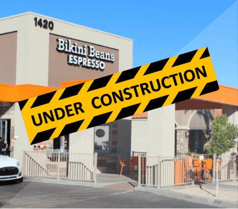 coffee shop that is a tan building with orange accents. Under construction banner accross the photo.