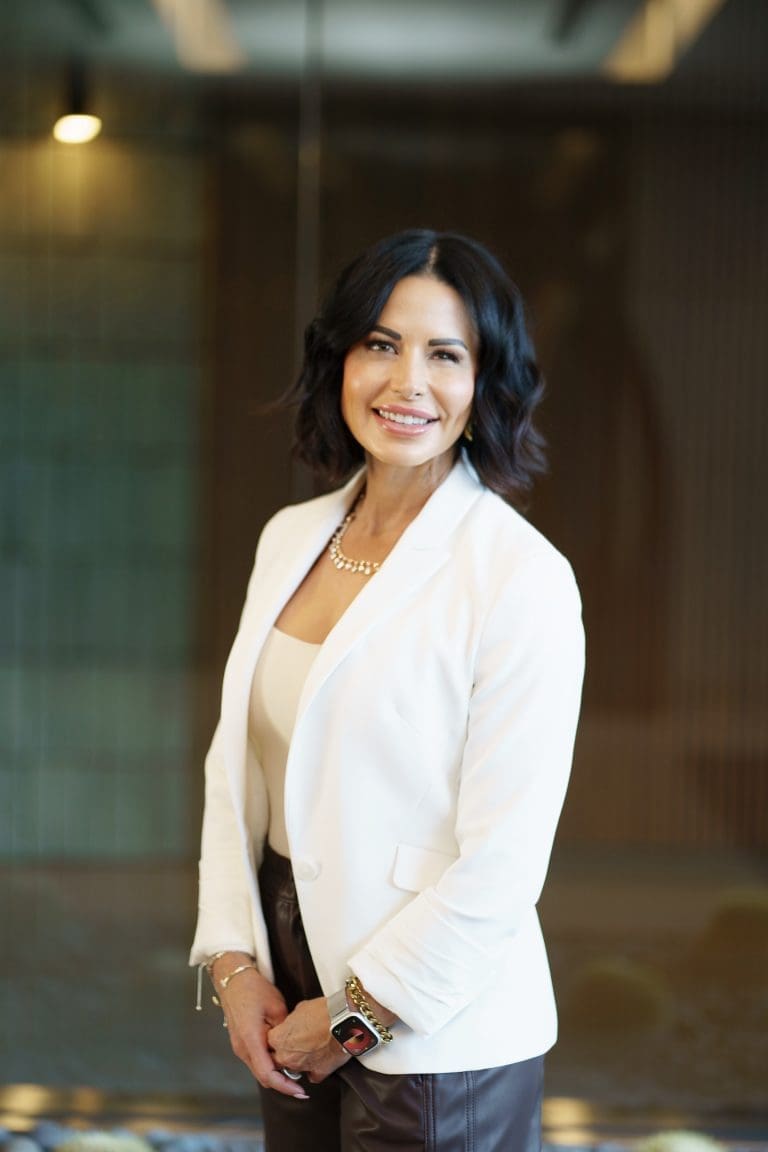 photo of Sheley Brien COO of Brien Contracting. She is wearing a cream blazer with brown pants and has short brown hair. The background is inside a building entrance.