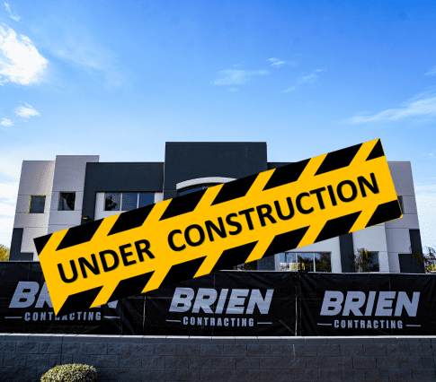 Exterior wide photo of two story construction project The Enclave in Scottsdale Arizona. Brien Contracting fence signage surrounding the building and parking lot. Also has a graphic Under Construction banner across photo.