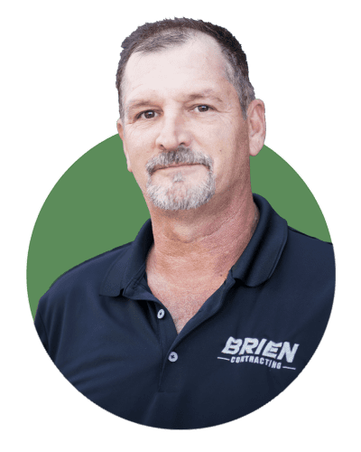 A middle-aged man with short hair and a goatee, wearing a dark polo shirt with the "Brien Contracting" logo—a trusted Arizona commercial contractor—stands in front of a green circular background.